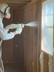 Person in respirator spray-painting an unfinished room near a covered window.