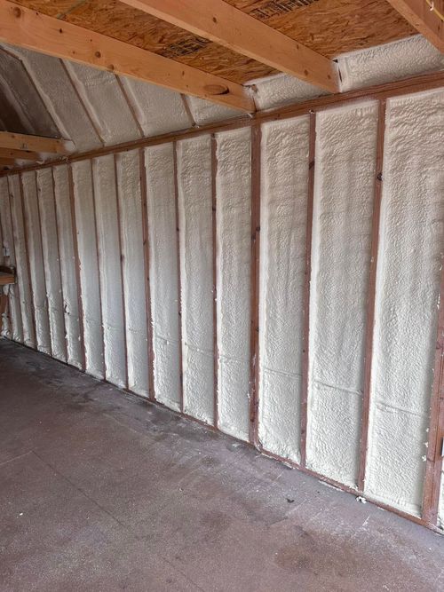Insulated attic wall with exposed wooden rafters and fiberboard panels.