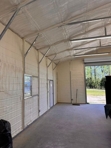 Empty metal-roofed garage with concrete floor, windows, and an open door to a sunny yard
