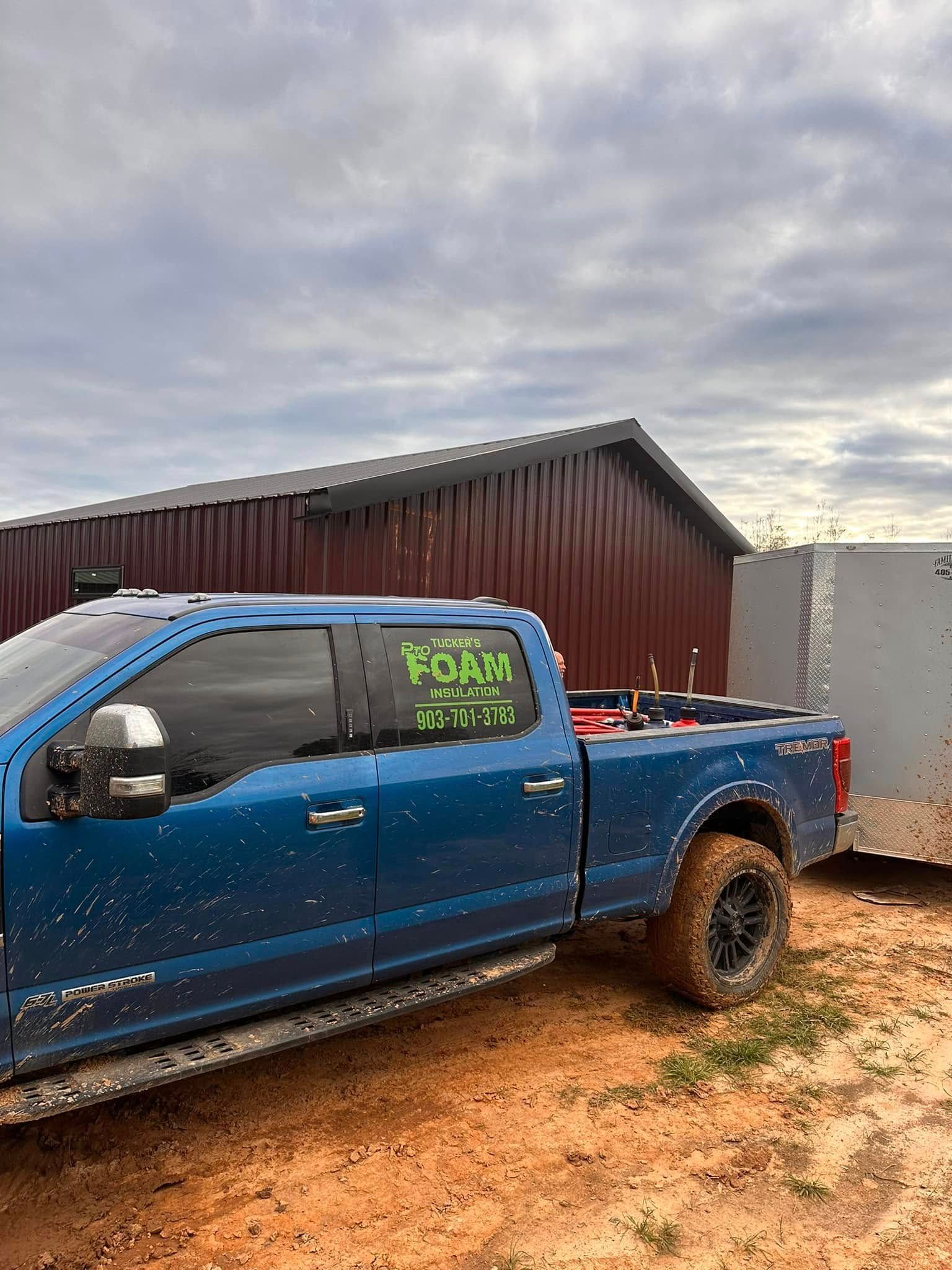 Blue pickup truck parked on muddy ground beside a barn under a cloudy sky