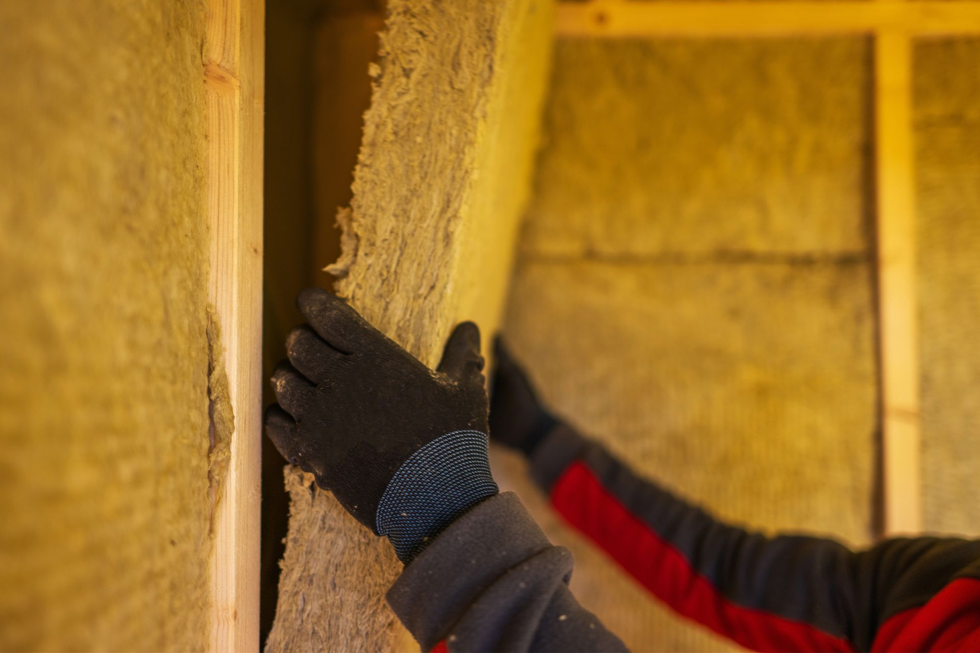 Gloved hands pressing insulation into a wall frame inside a building under construction
