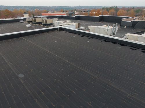 Flat black rooftop with HVAC units and autumn trees in the distance