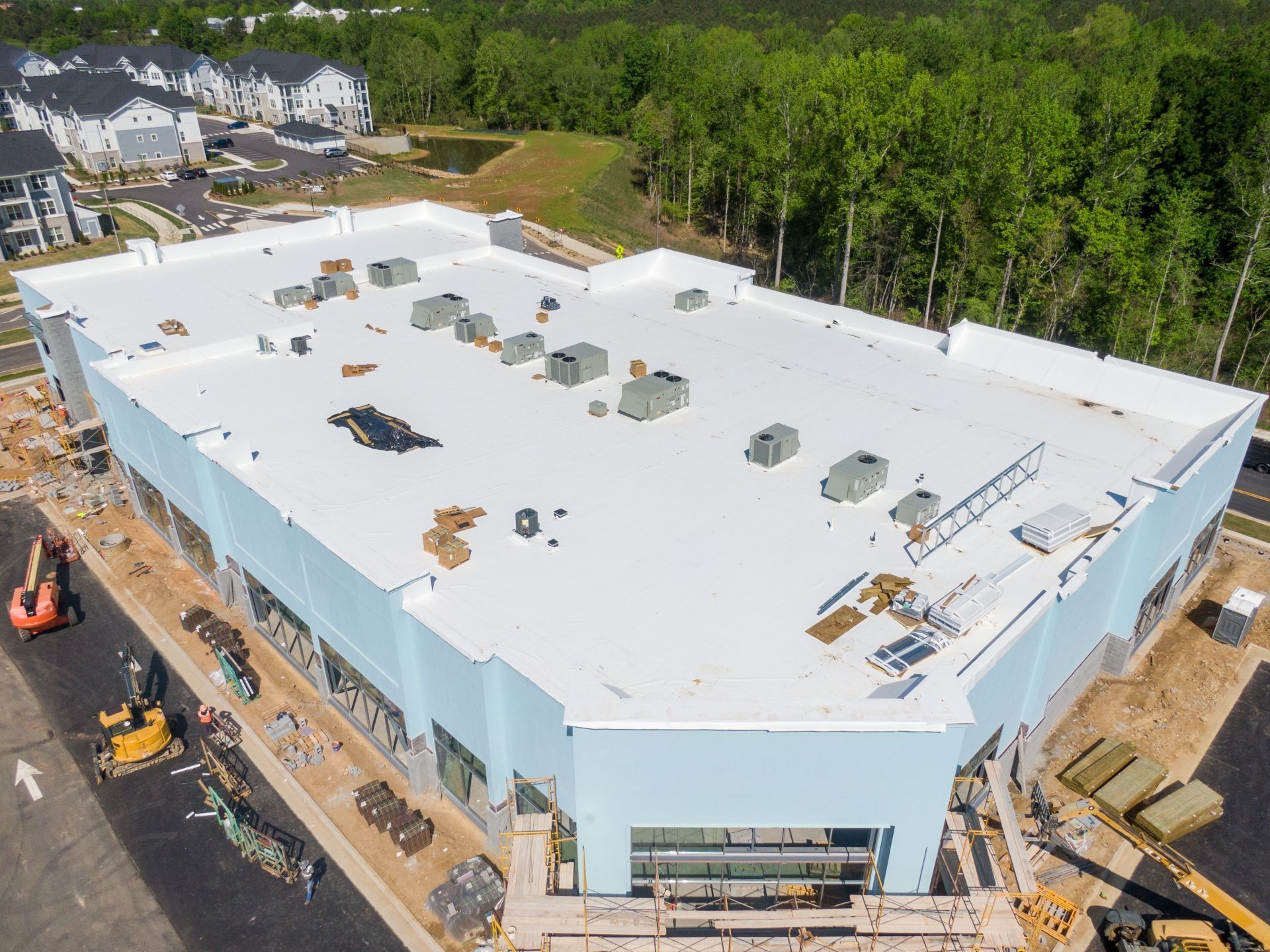 Aerial view of a large white-roofed building under construction beside a wooded area.