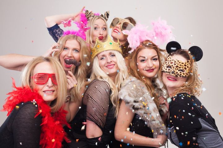 Group of people in colorful wigs and costumes posing together at a party, smiling at the camera.