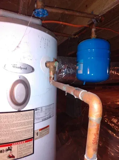 A white Whirlpool water heater with a blue expansion tank connected by copper pipes.