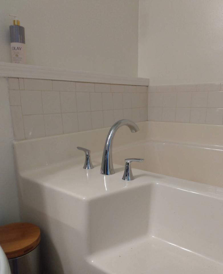 A white bathtub with chrome faucet and handles, built-in in a bathroom with white walls and a shelf.