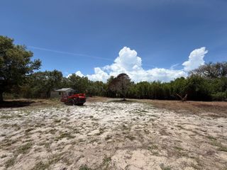 Red tractor on a sandy clearing under a bright blue sky with scattered clouds, bordered by trees