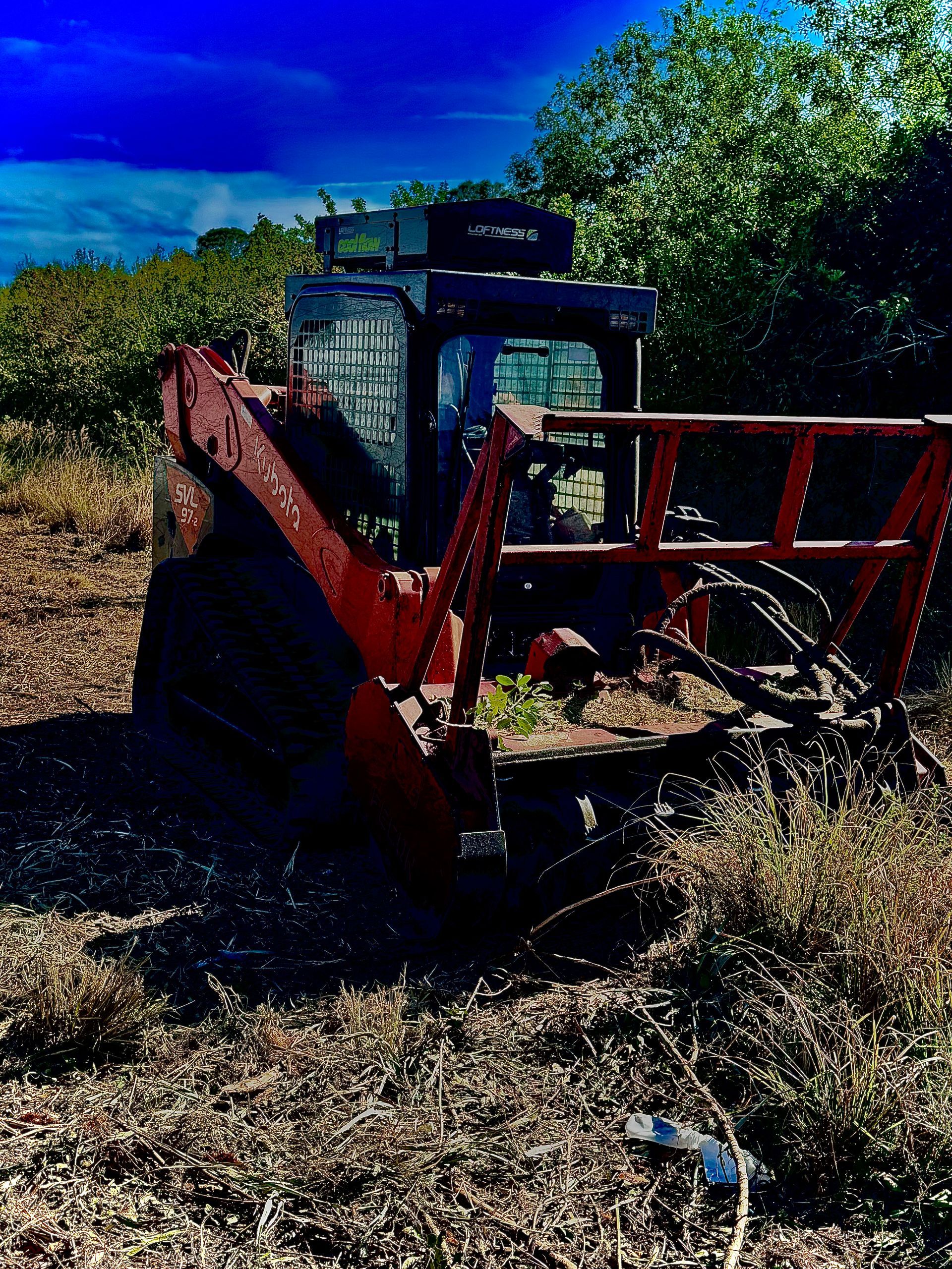 Rusty red tractor in a dry field with trees and blue sky in the background