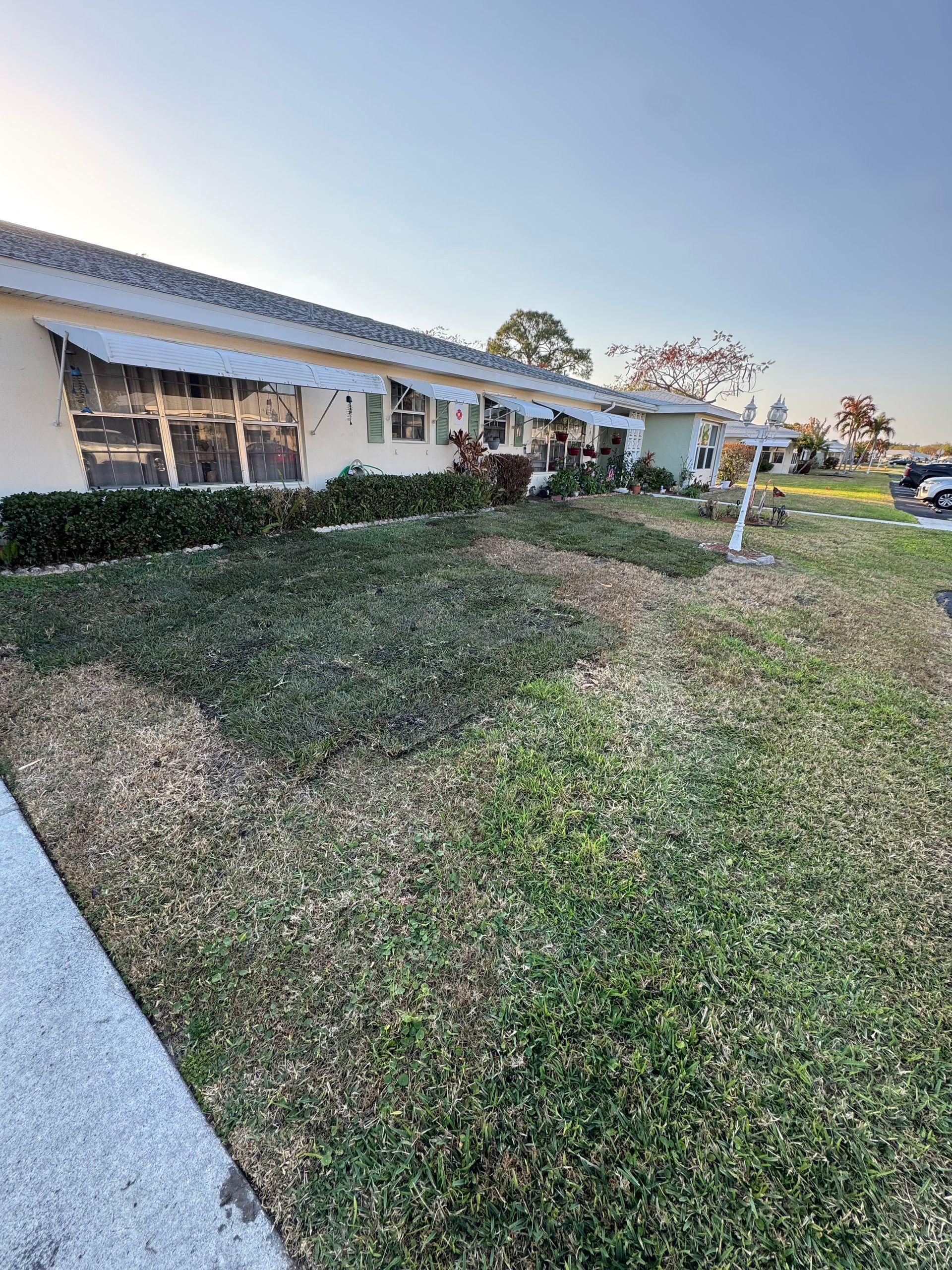 Single-story white house with a sloped lawn, screened porch, and parked car in the driveway.