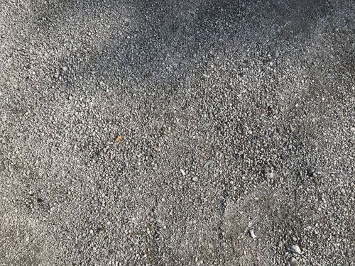 Gray gravel or textured asphalt surface with small pebbles and specks scattered across it