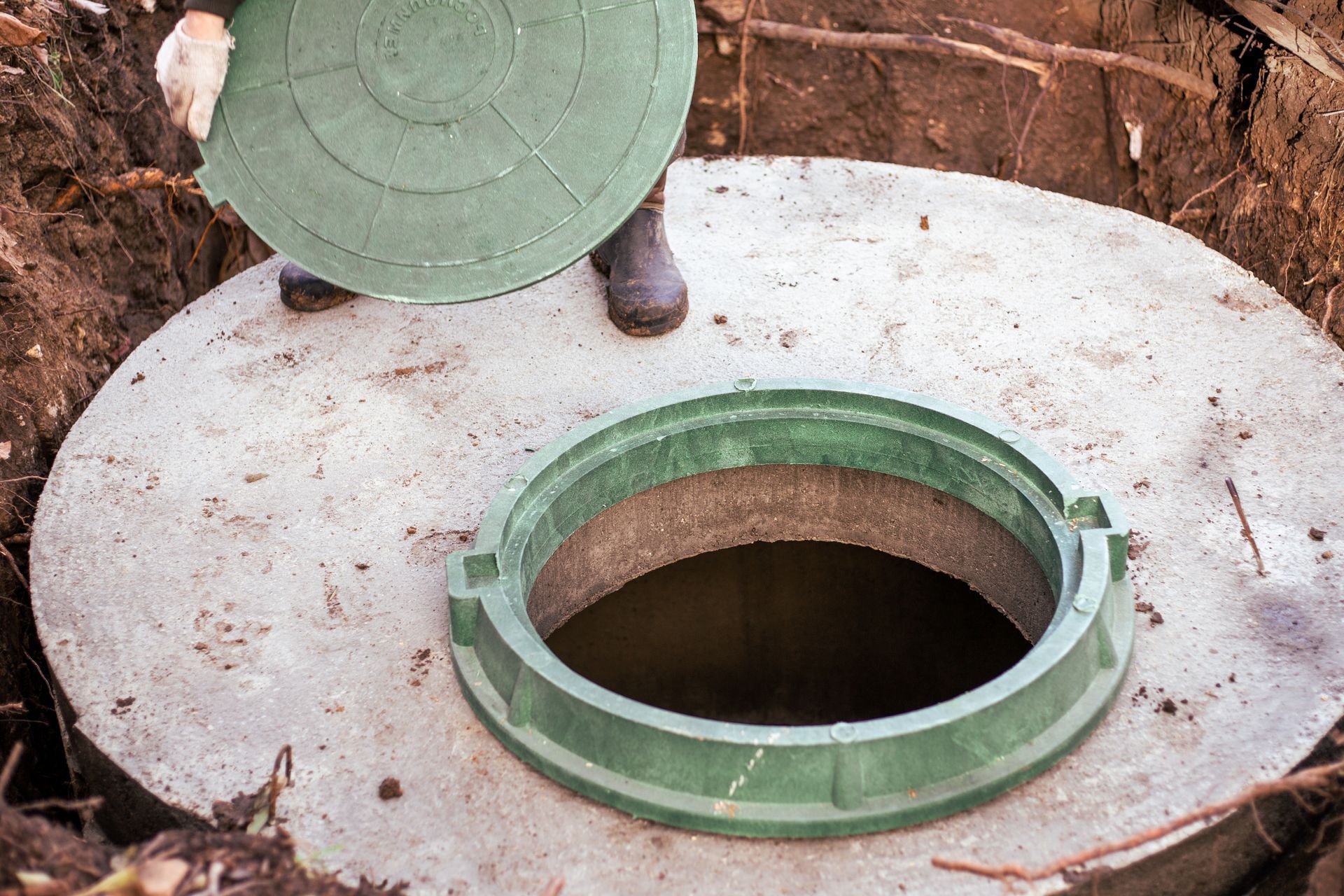 A person lifts the lid of a concrete septic tank, revealing the opening.