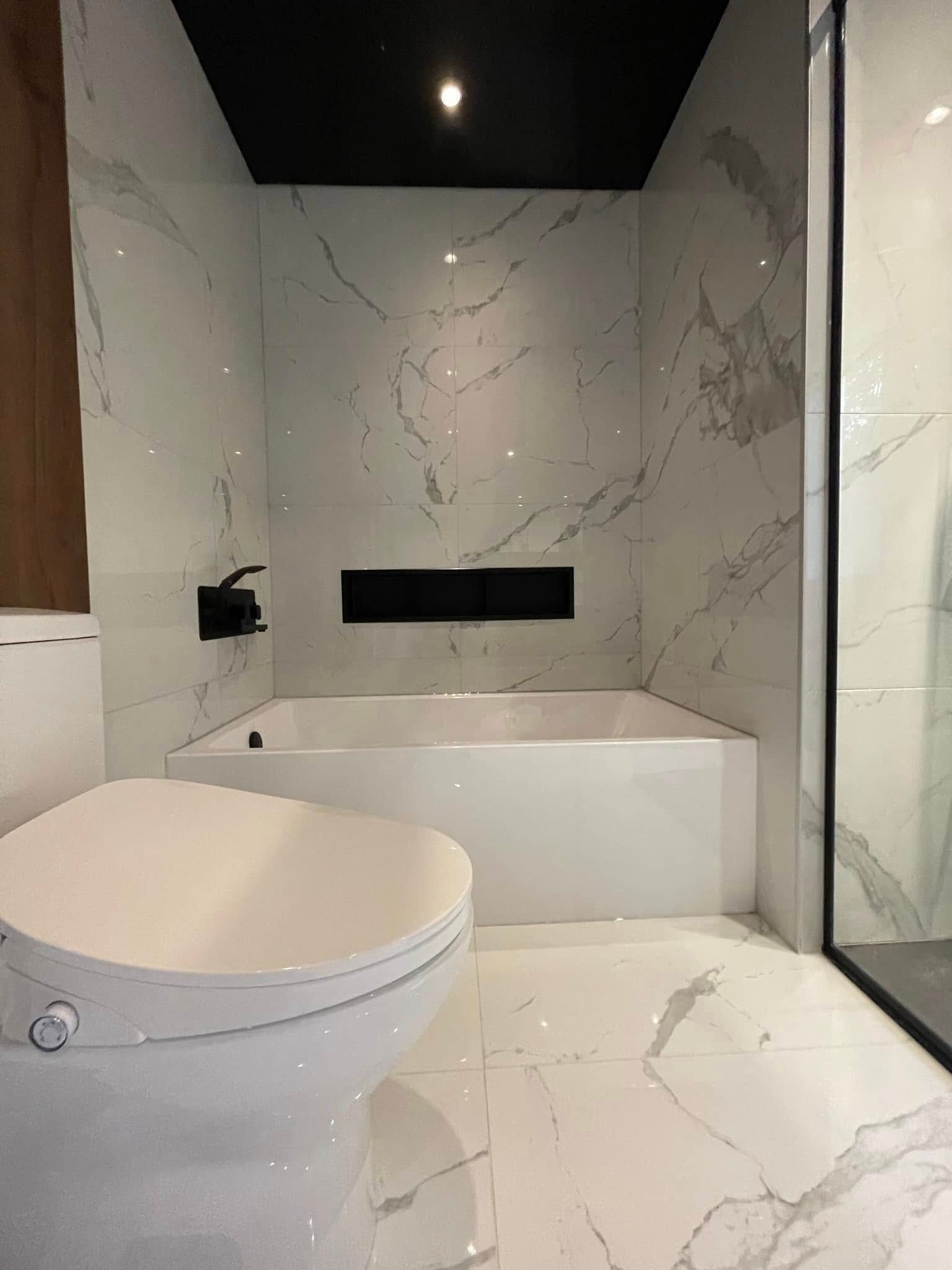 Salle de bains moderne avec carrelage en marbre blanc, robinetterie noire et baignoire.