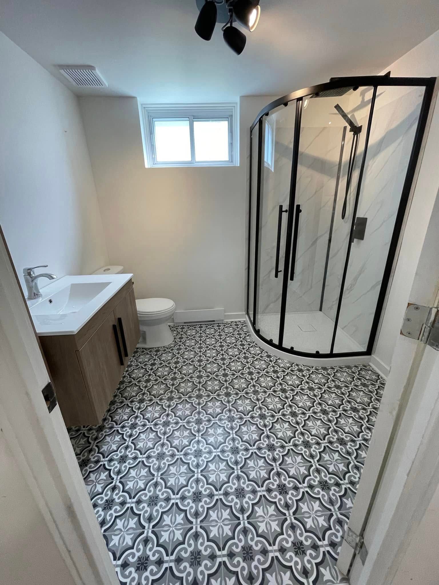 Salle de bains avec sol carrelé à motifs, douche en verre, meuble-lavabo et toilettes.