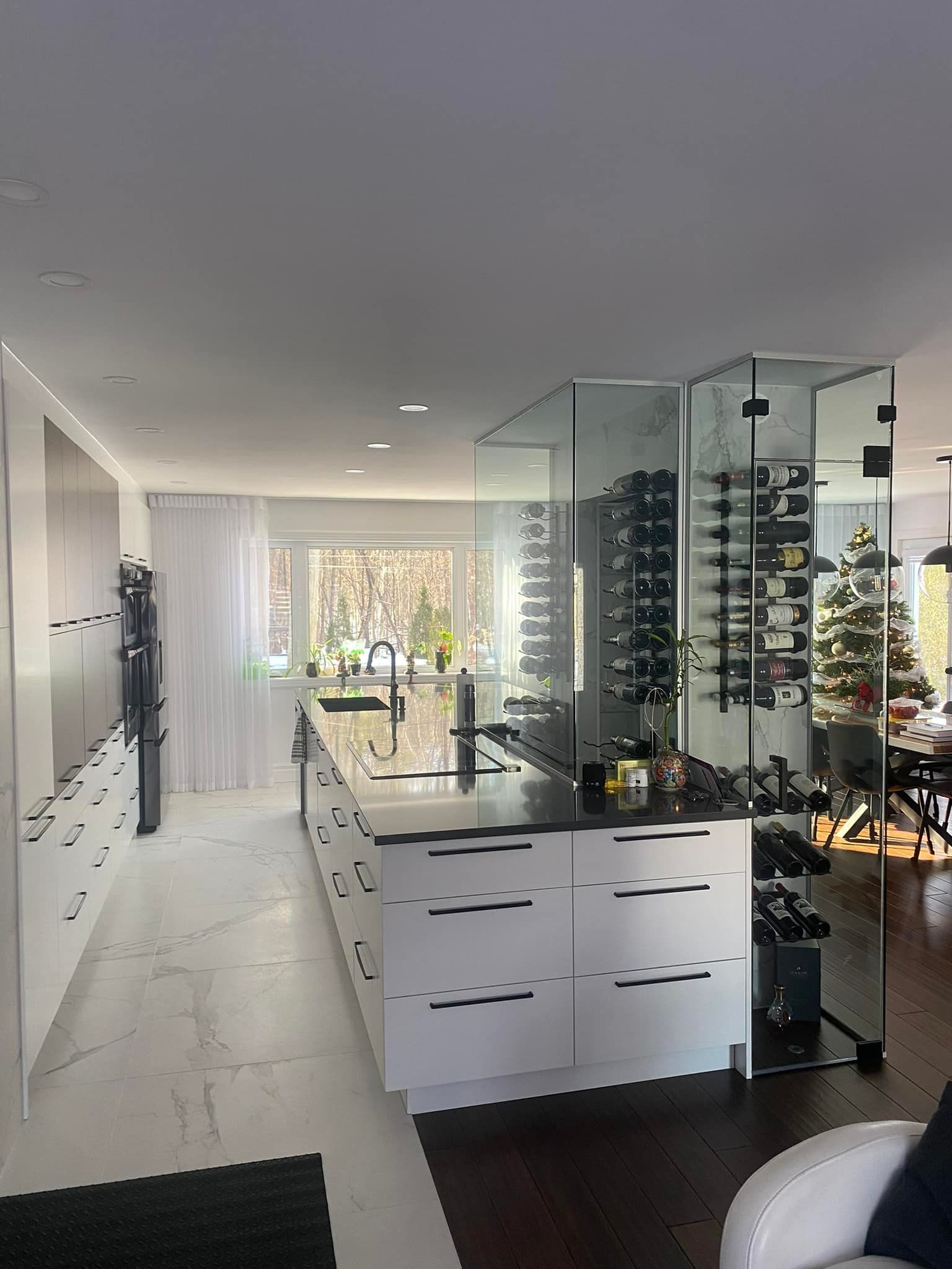Cuisine moderne avec îlot central en plan de travail noir, placards blancs et casier à vin en verre.
