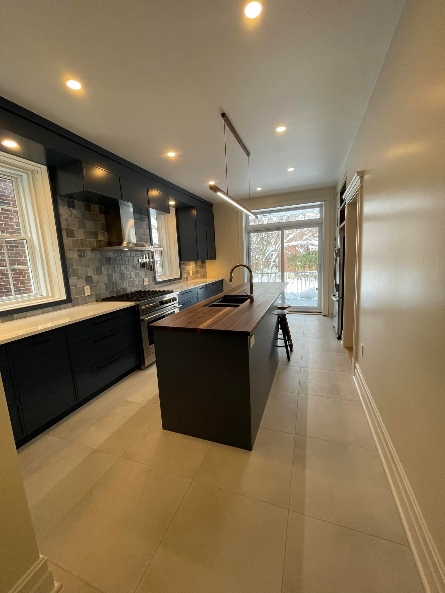 Cuisine moderne avec placards noirs, îlot central et plan de travail en bois ; sol clair.