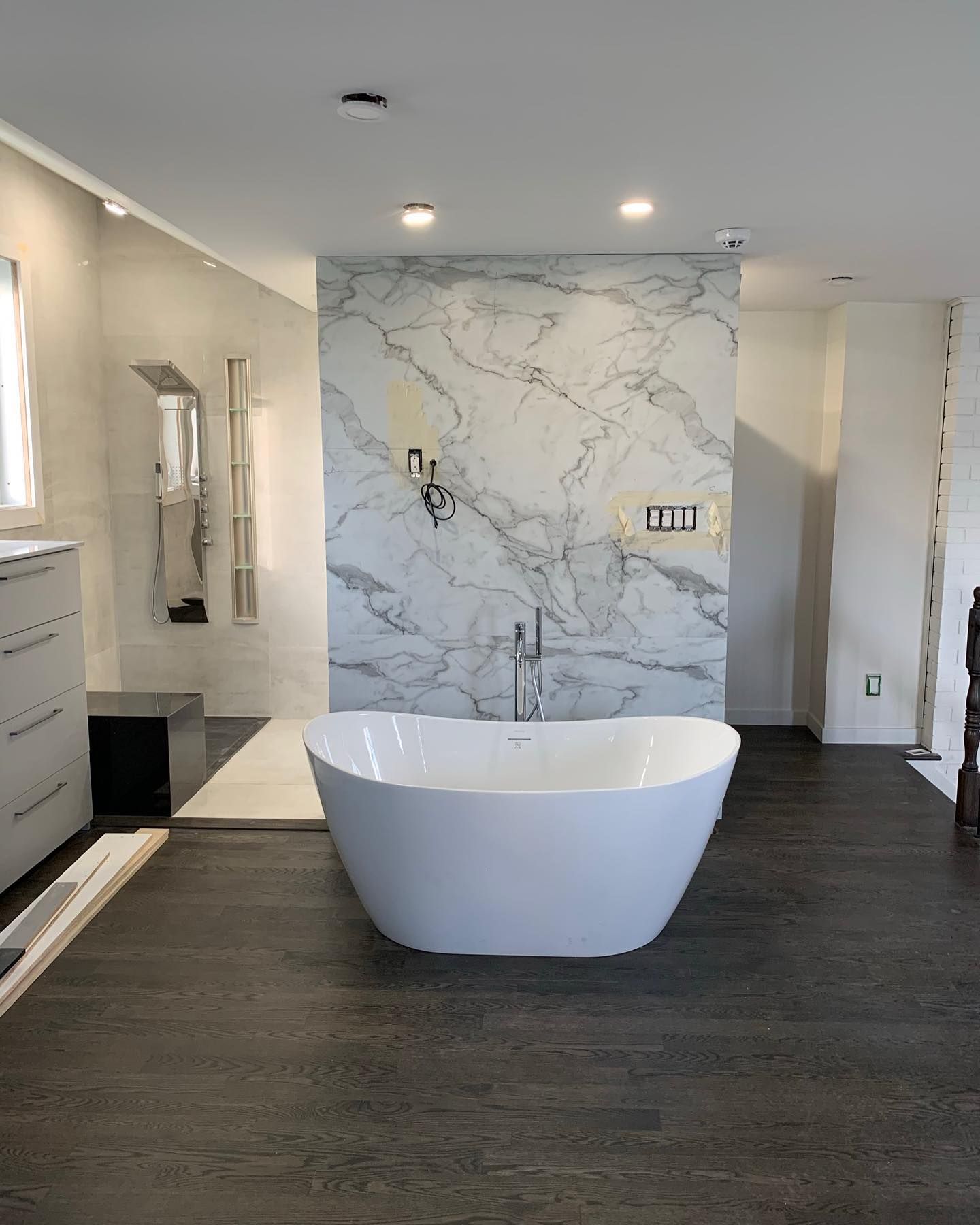 Salle de bains moderne avec baignoire îlot blanche, mur d'accent en marbre et sol gris foncé.