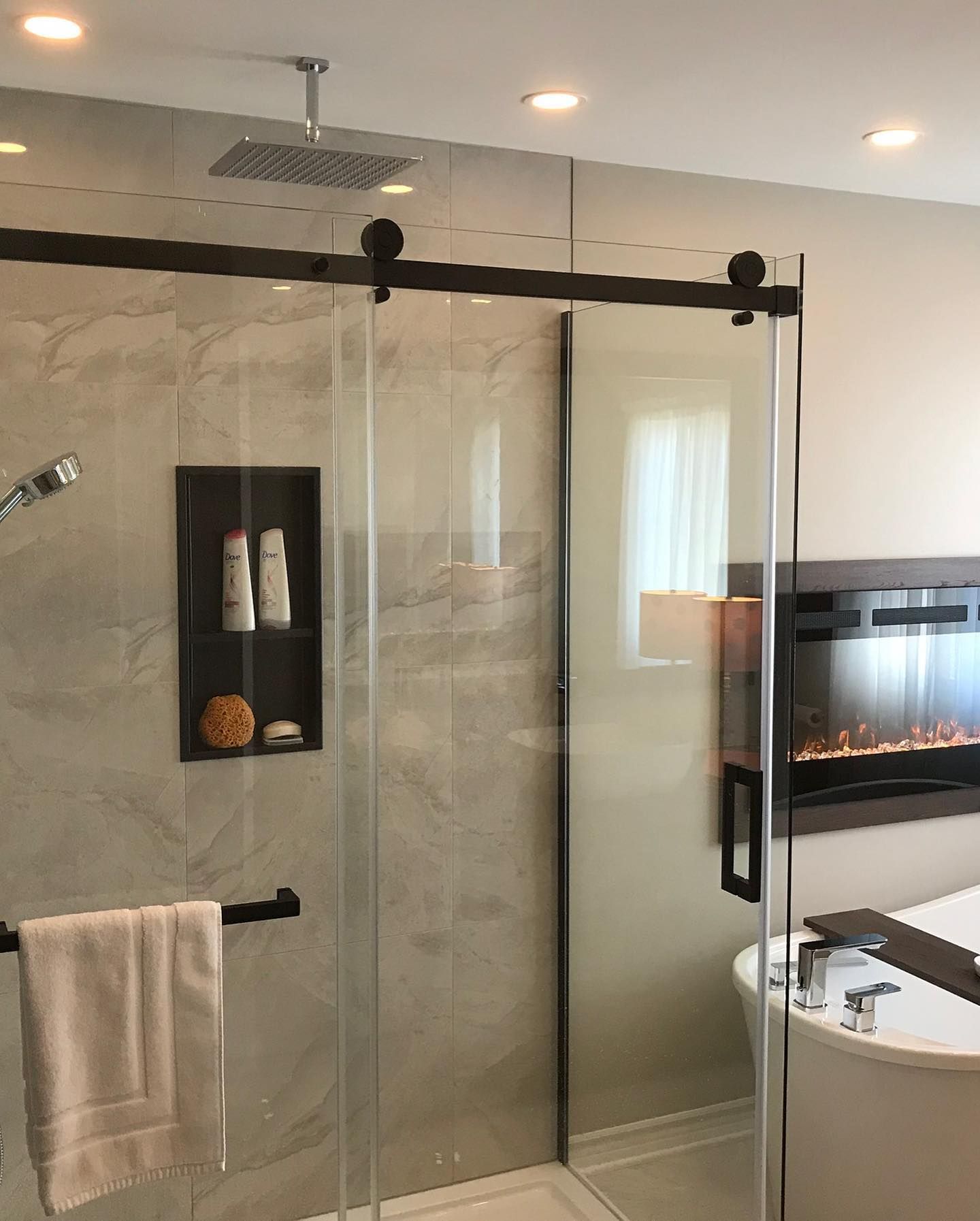 Salle de bains moderne avec paroi de douche en verre, robinetterie foncée et étagère intégrée.