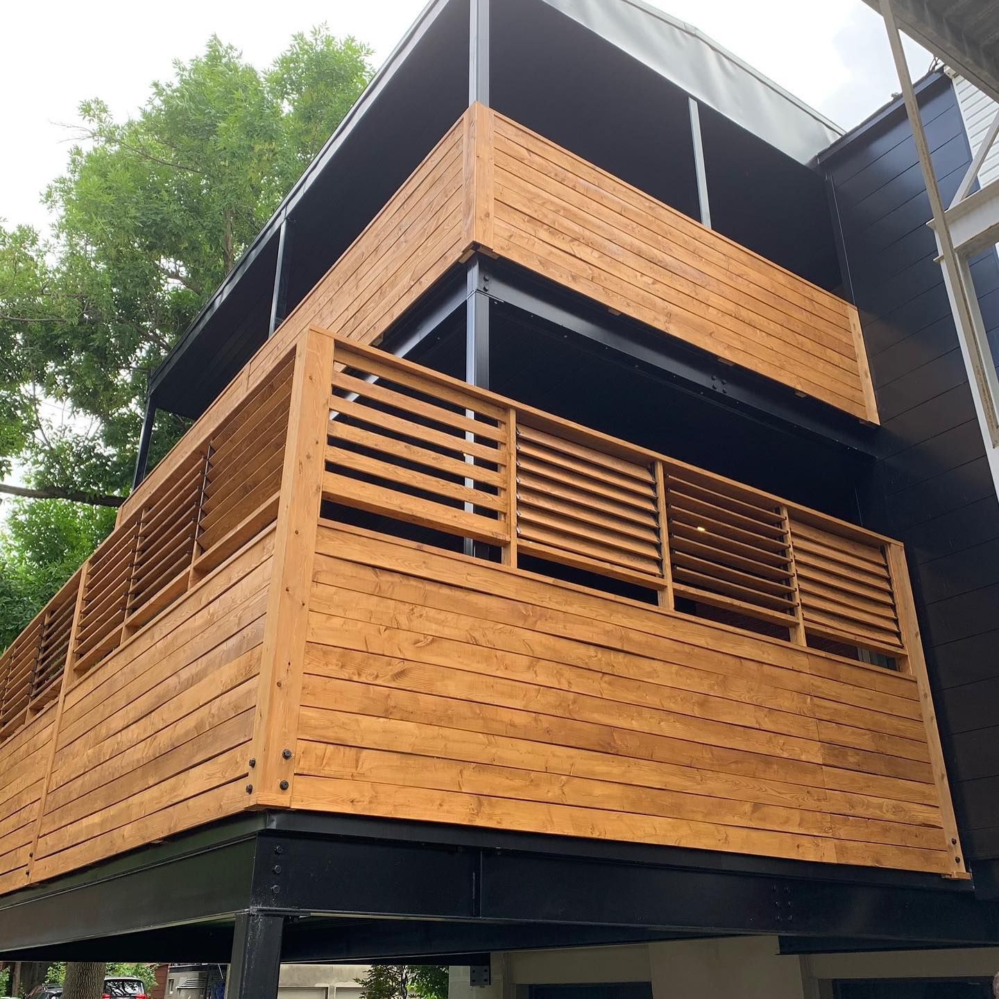 Bâtiment de deux étages avec balcons en bois et supports noirs ; journée nuageuse.