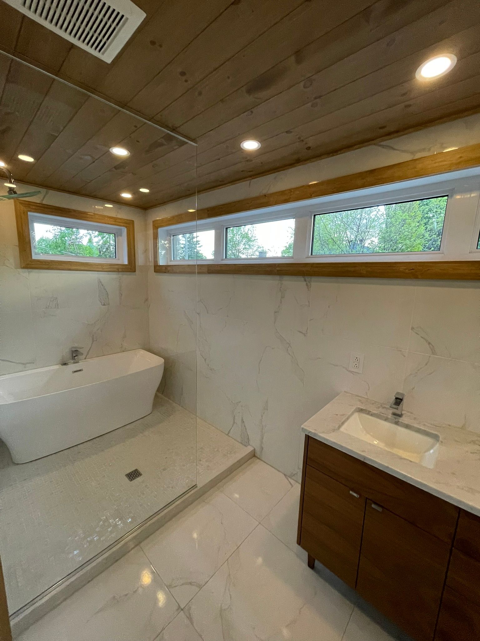 Salle de bains moderne avec carrelage en marbre blanc, éléments en bois et baignoire îlot.