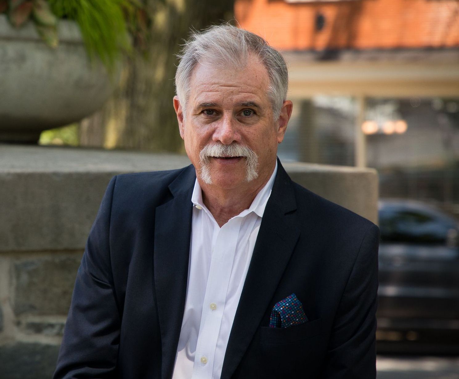 A man in a suit and white shirt is sitting on a stone wall.