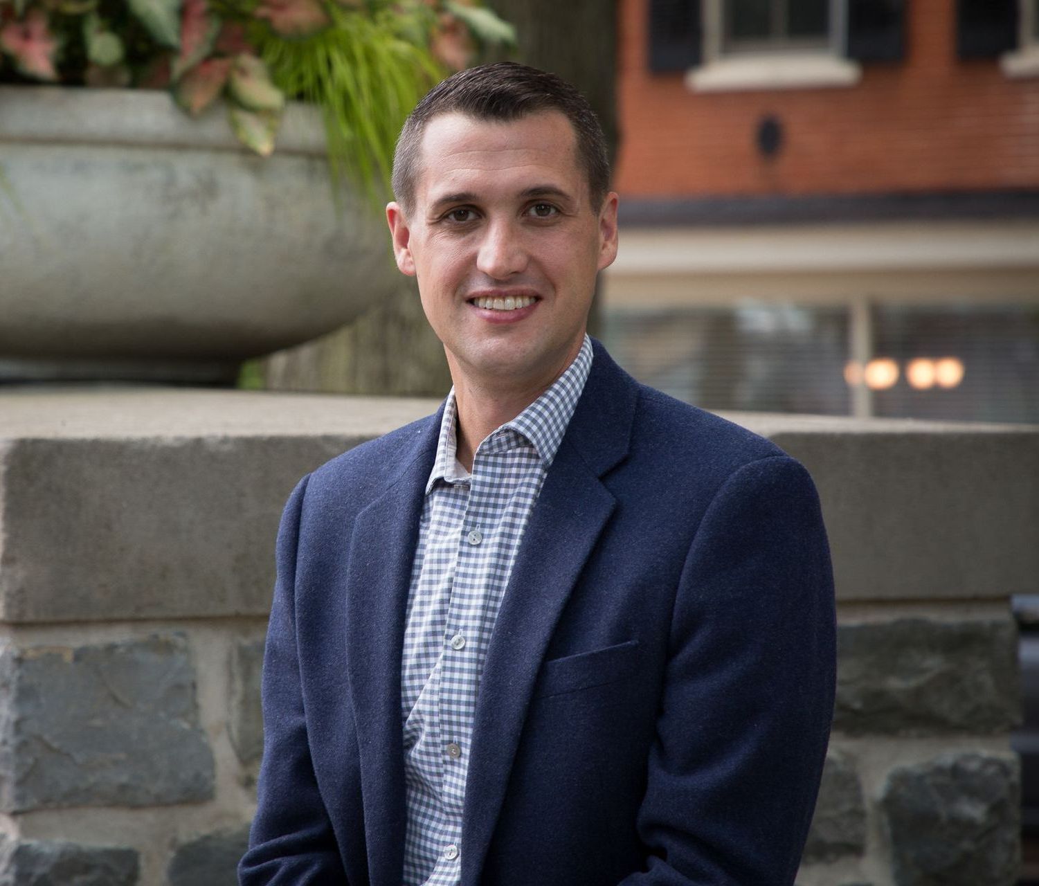 A man in a suit and plaid shirt is sitting on a stone wall.