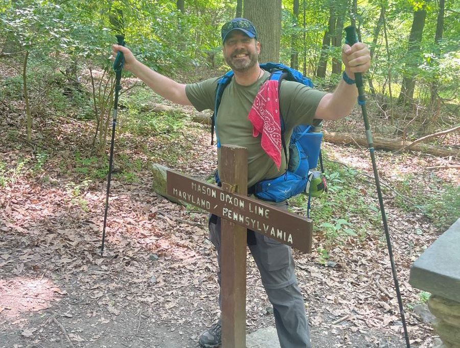 A man with a backpack is standing next to a sign in the woods.