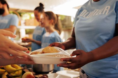 A woman in a blue shirt is serving food to another woman.