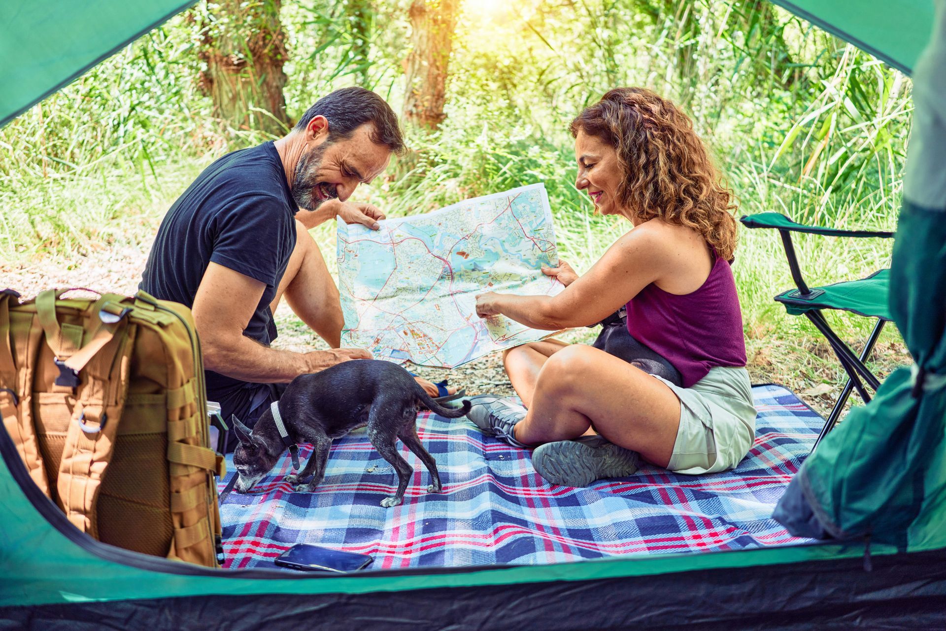 A man and a woman are sitting on a blanket in a tent looking at a map.