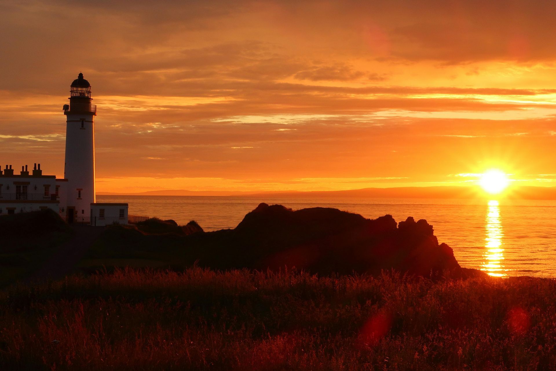 A lighthouse is silhouetted against a sunset over the ocean.