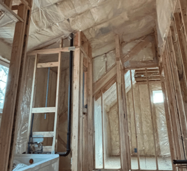 Interior of a house under construction with exposed insulation, wood framing, and a ladder in the center.
