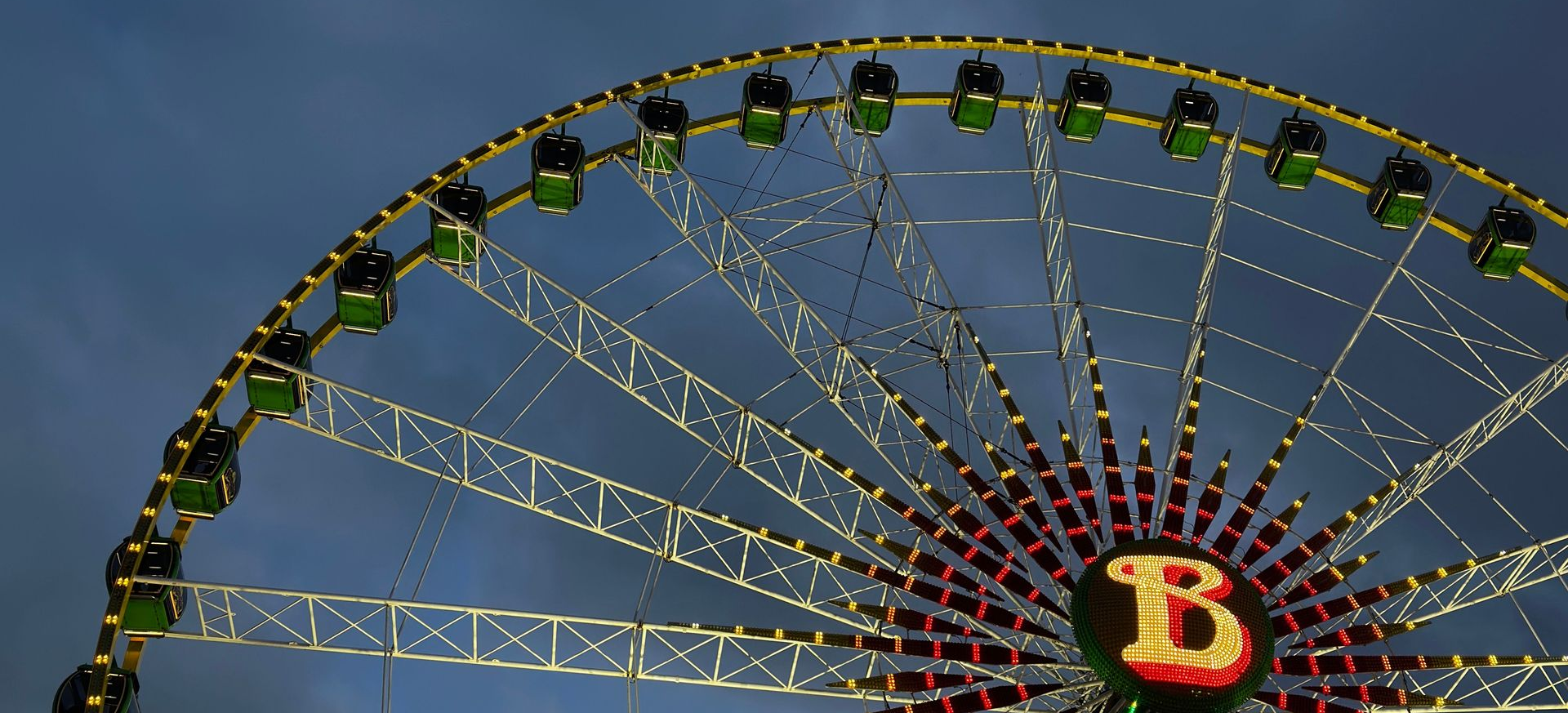 Ferris wheel against a twilight sky, with a lit red-yellow “B” at the center