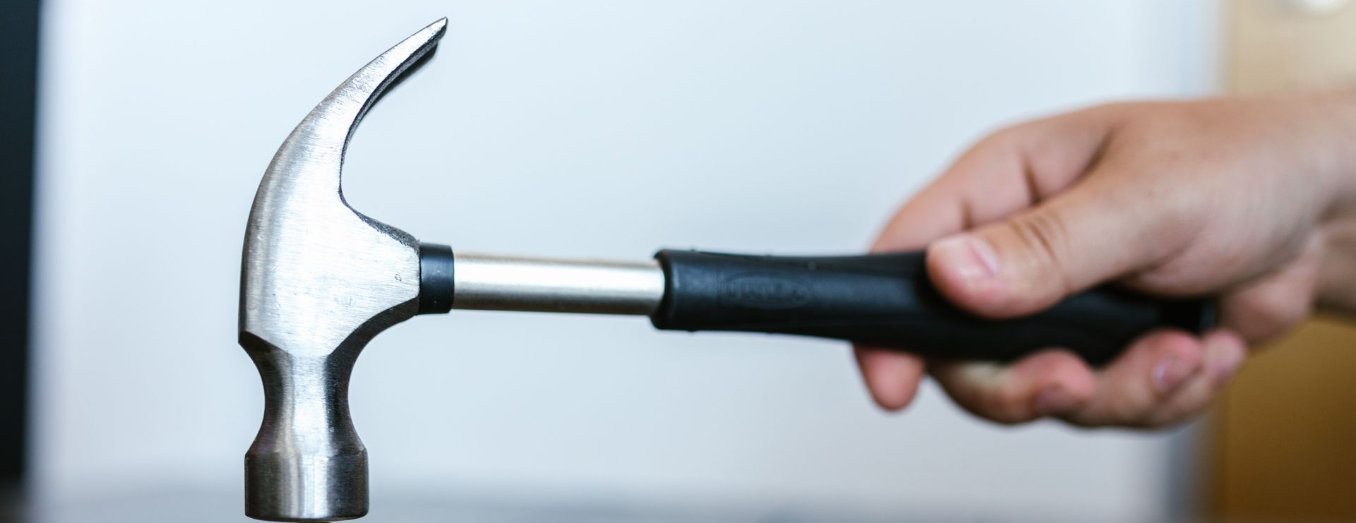 Hand holding a hammer striking a silver nail against a white wall