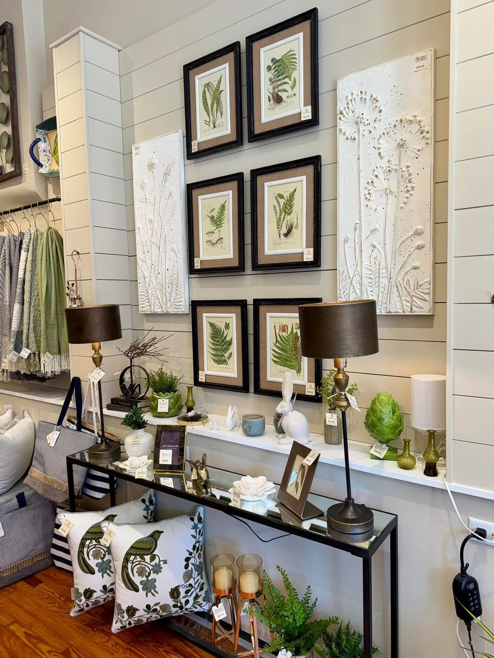 Decorative shelves and framed botanical art above a console table in a bright living room