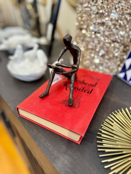 Small dark figurine seated on a red book on a tabletop with glittery decor nearby