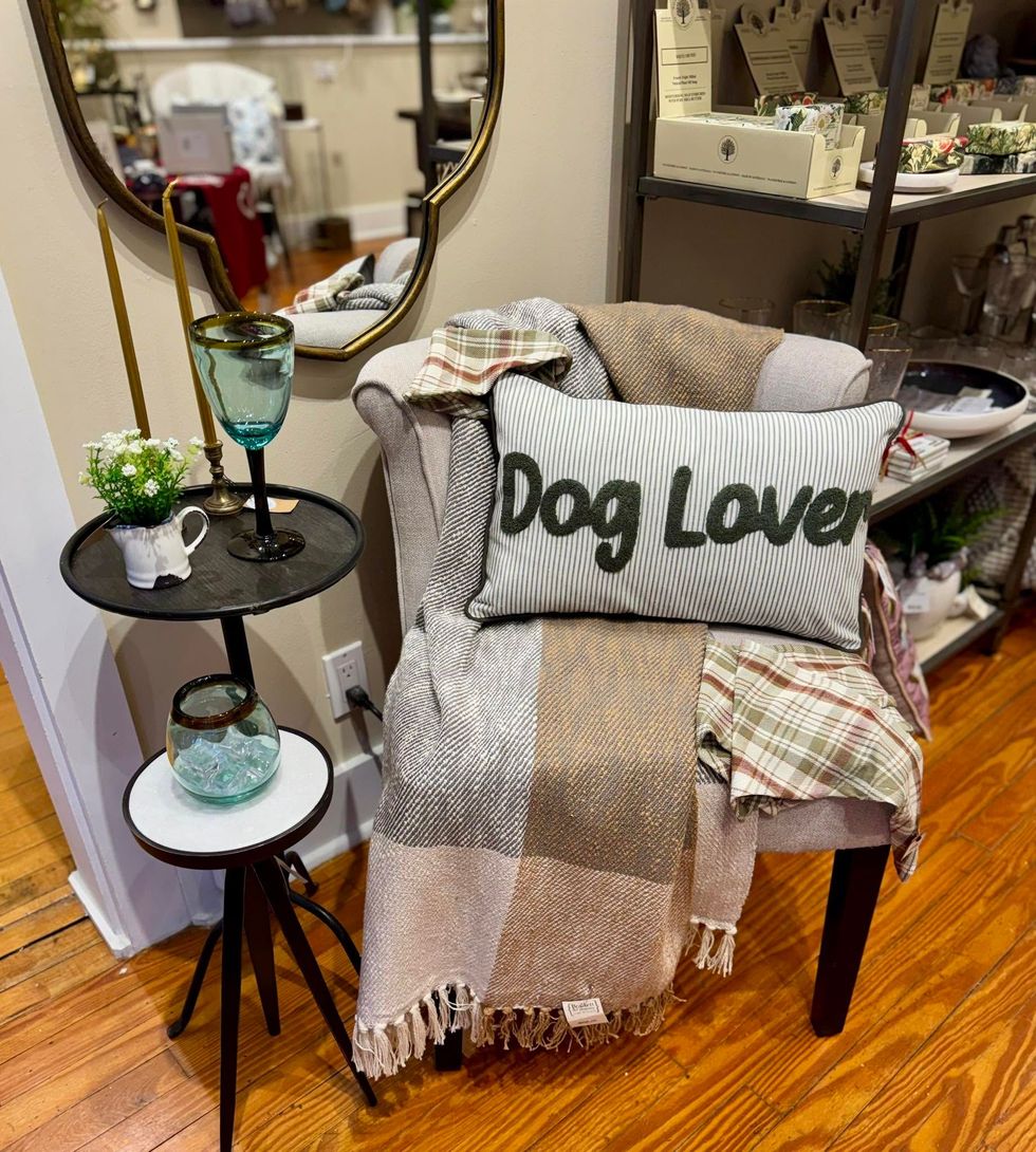 Cozy chair with plaid throw and “Dog Lover” pillow beside a round side table in a home decor shop