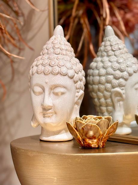 White Buddha statue beside a gold candle holder with a lotus on a bronze surface