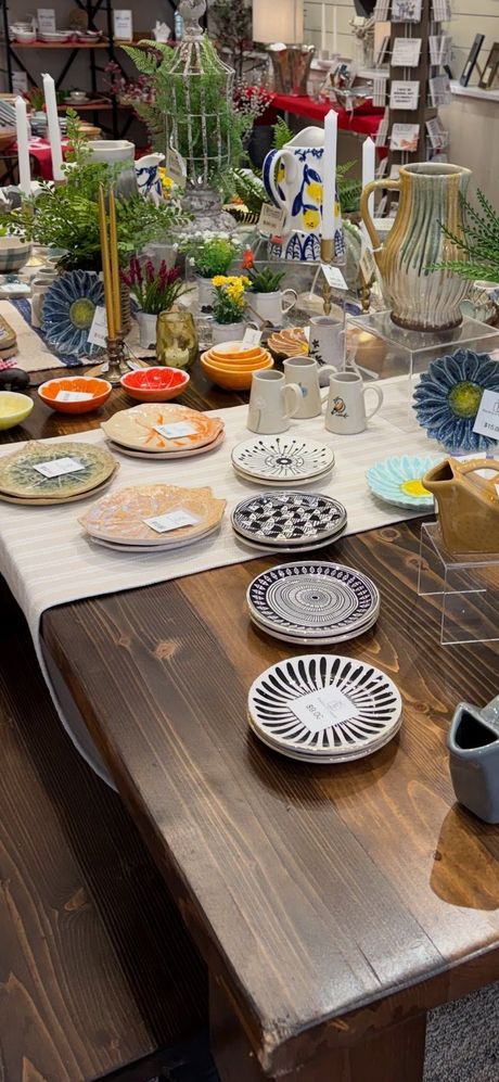 Display of colorful ceramic dishes and glassware on a market table with flowers and decor