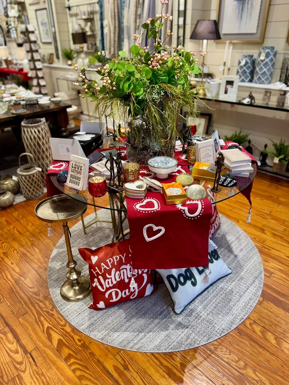 Festive red Valentine’s Day table display with flowers, cakes, and gifts on a round rug