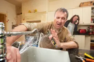 Kitchen & Bath Highlands Plumbing Ranch CO Man fixing a sink in a kitchen, water spraying everywhere, while a woman watches in the background