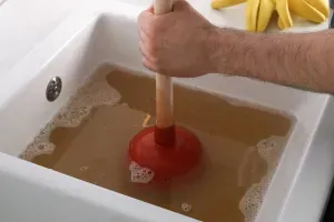 Drain Cleaning Castle Pines, CO Person using a plunger in a clogged sink with dirty water
