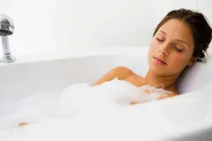 Water Heaters Castle Pines, CO Woman relaxing in a bubble bath with eyes closed in a white bathtub