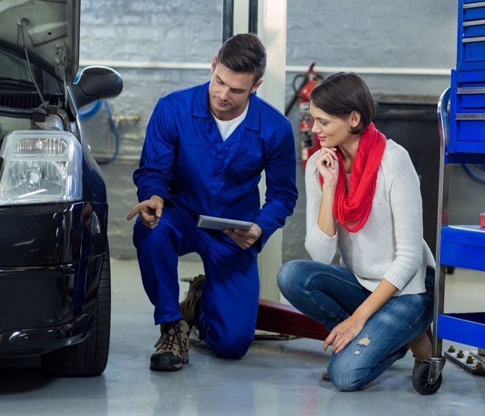 A man and a woman are looking at a car in a garage.
