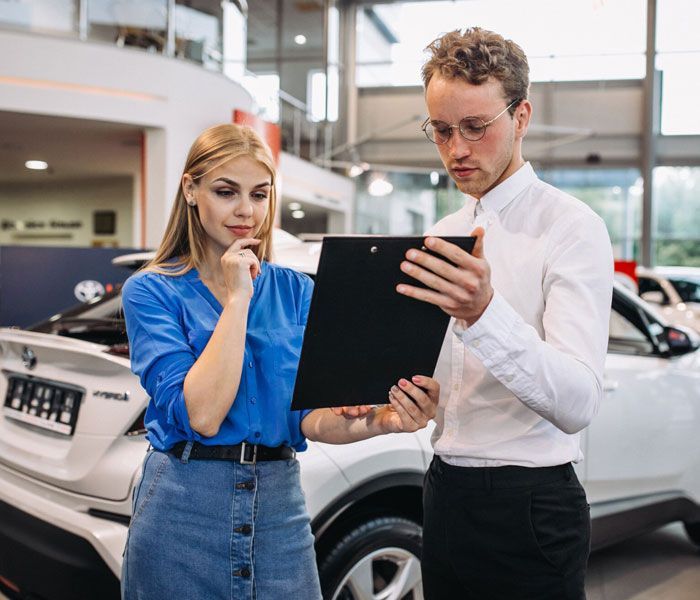 A man and a woman are looking at a tablet in a car showroom.