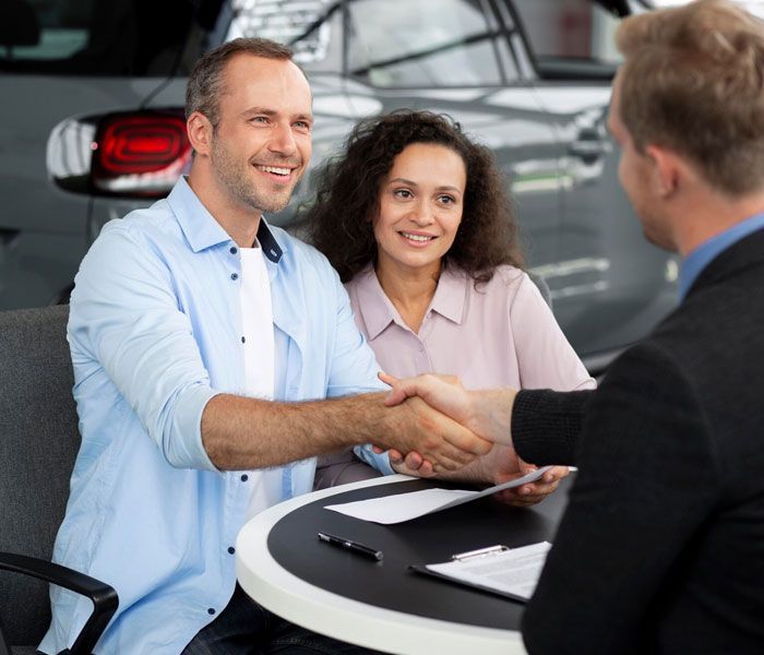 A man and woman are shaking hands with a car dealer.