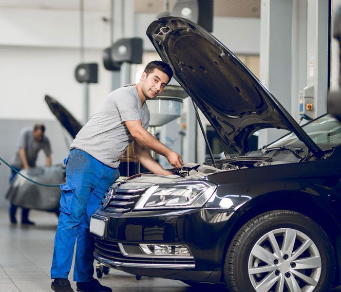 A man is working on a car in a garage with the hood open.