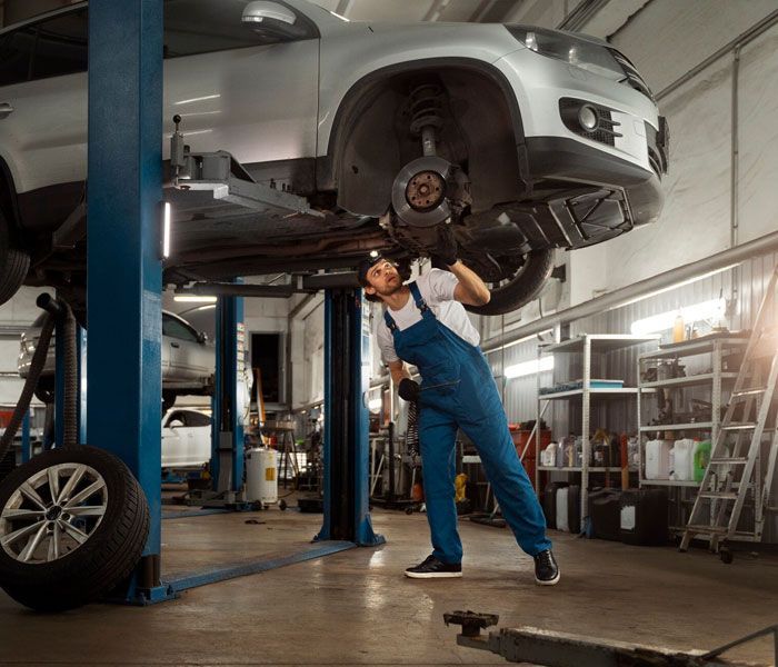 A man is working on a car on a lift in a garage.