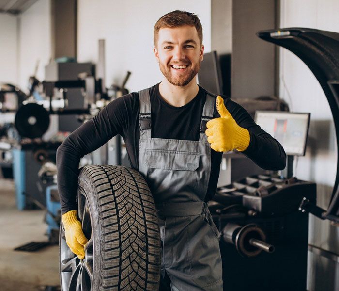 A man is holding a tire in a garage and giving a thumbs up.