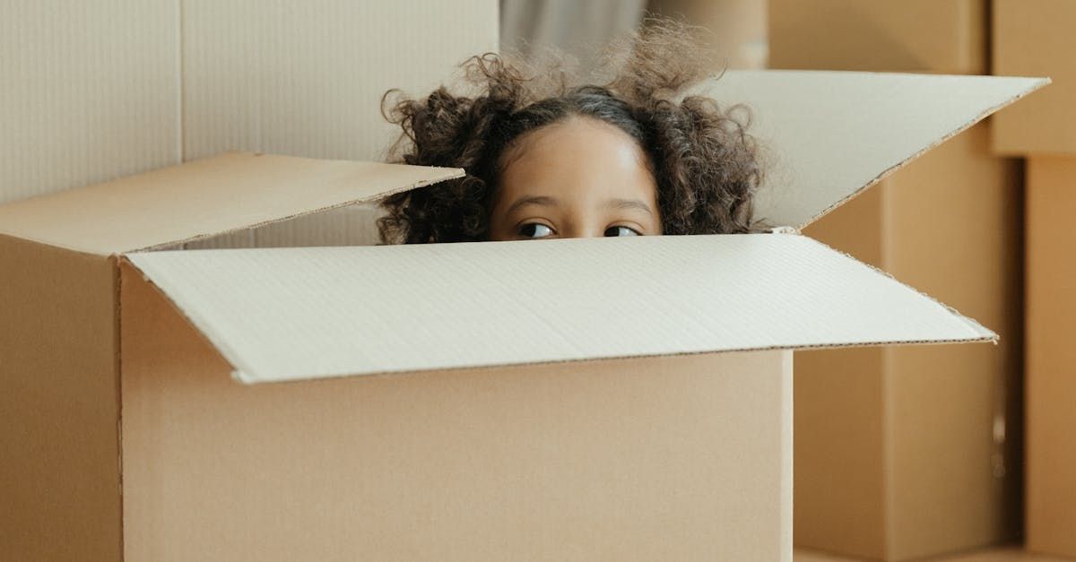 A woman is peeking out of a cardboard box.