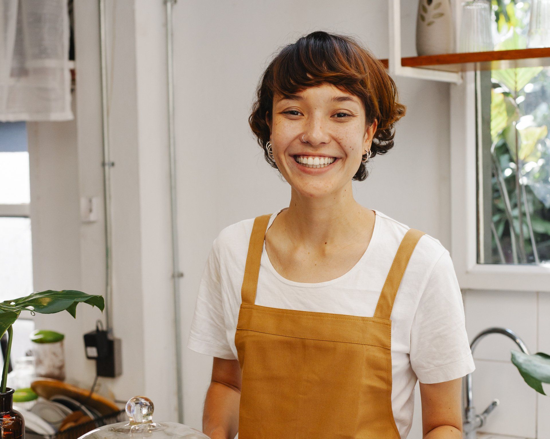 A woman in an apron is smiling in a kitchen.