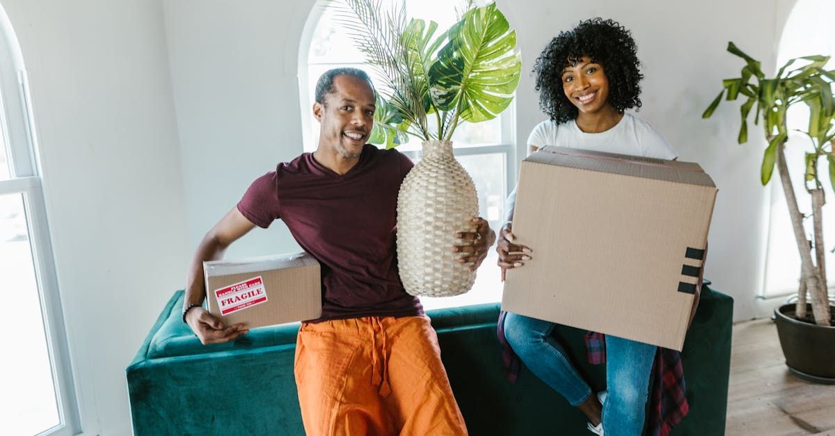 A man and a woman are sitting on a couch holding boxes and a vase.